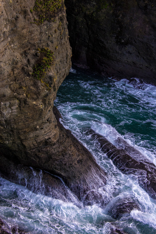Looking down into a narrow rocky sea canyon as turquoise water surges between dark cliff walls